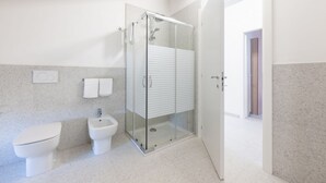 Moderni kylpyhuone, jossa on lasiseinällä varustettu suihku, wc ja bidee.