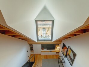 A room with a sloped ceiling, a skylight, wooden beams, a staircase, and a flat-screen TV. - ELEGANT DOWNTOWN APARTMENT by VACATIONY by Interhome (Porto)