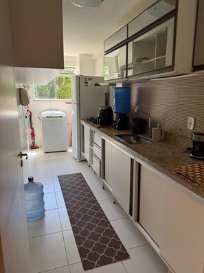 A modern kitchen with white cabinets, a granite countertop, a large water dispenser, and a view of the outdoors. - Beachfront apartment in Recreio (Rio de Janeiro)