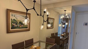 Comedor con mesa de vidrio, sillas de mimbre e iluminación colgante.