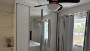 Hotellihuone, jossa on sänky, kattotuuletin, ikkuna verhoilla ja ovi, joka johtaa toiseen huoneeseen.