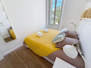 Ein Schlafzimmer mit einem Bett, einer Nachttischlampe, einem Spiegel und einem Fenster.