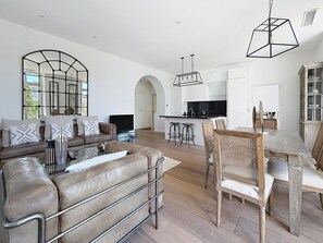 Ein modernes Wohnzimmer mit einer Ledersofa, einem Essbereich mit Holztisch und einer Küche mit weißen Schränken.