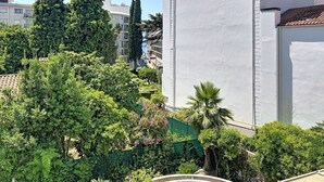 Un quartiere residenziale con un edificio bianco, vegetazione rigogliosa e cielo sereno.