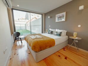 A modern bedroom with a large bed, a chair, a small table, and a view of the outside. - Apartment  by Interhome (Porto)