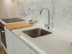 A kitchen with a stainless steel sink, a wooden cutting board, a bowl with utensils, and a modern faucet. - Apartment  by Interhome (Porto)