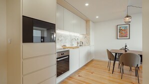 Una cocina moderna con armarios blancos, horno integrado y una mesa de comedor de madera con sillas.