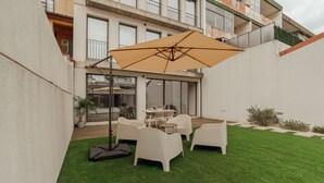 Un patio con zona de comedor, que incluye una mesa y sillas, y un paraguas grande.