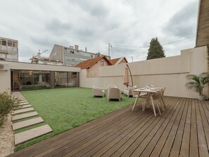 Eine moderne Außenpatio mit Holzterrasse, einem kleinen Rasenbereich und einer Sitzgruppe.