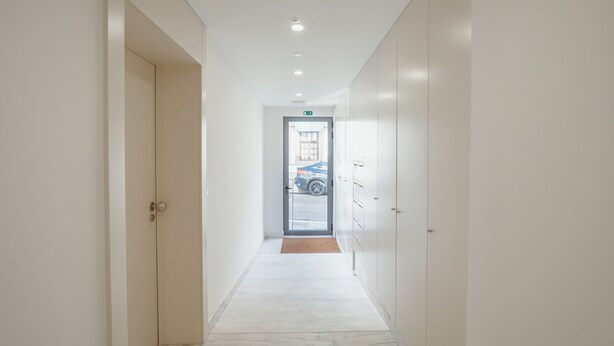 Un pasillo con una puerta a la izquierda, otra a la derecha, y una vista al exterior a través de un acceso de vidrio al final.