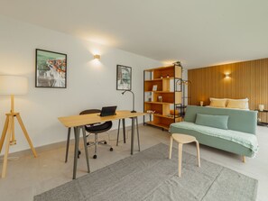 Ein modernes Wohnzimmer mit Schreibtisch, einer Couch, einem Bücherregal und einer Lampe.