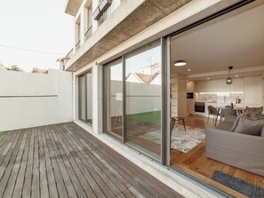 A modern apartment with a wooden deck, a sliding glass door leading to a living area with a sofa, a kitchen, and a dining table. - Apartment  by Interhome (Porto)