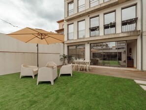 A patio area with a table and chairs, a large umbrella, and a building with balconies in the background. - Apartment  by Interhome (Porto)