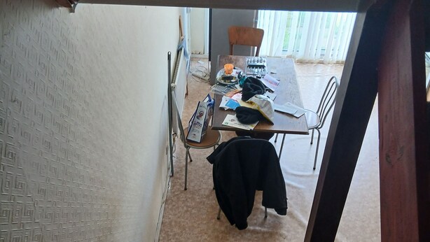 A staircase leading to a room with a patterned wall, a table with various items, and a chair. - Room-room in a Family House (Grays)