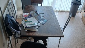 A cluttered room with a table covered in papers and magazines, a chair with a jacket, and a radiator. - Room-room in a Family House (Grays)