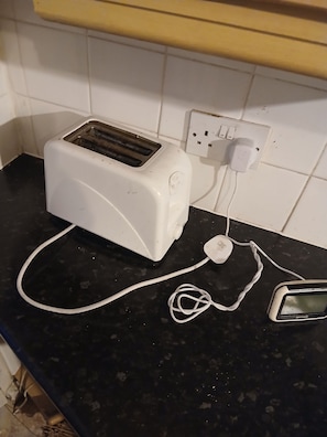 A white toaster on a black countertop with a power outlet and a white cord. - Room-room in a Family House (Grays)
