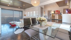 A modern living room with a glass dining table, a sofa, and a chandelier.