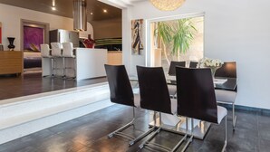 A modern dining area with a glass table, black chairs, and a hanging light fixture.