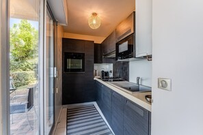 Une cuisine moderne avec des meubles de rangement aux couleurs sombres, un évier en acier inoxydable et un four à micro-ondes encastré.