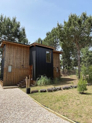 A rustic cabin with a wooden exterior, a black door, and a gravel driveway.
