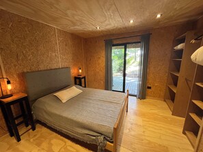 Une chambre Ă coucher comprenant un lit, un plancher en bois, une table de chevet avec une lampe, une porte-fenĂȘtre coulissante donnant sur un patio et une bibliothĂšque intĂ©grĂ©e.