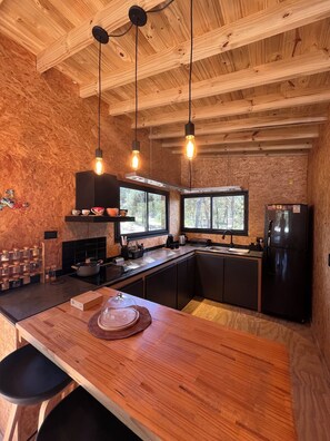 A modern kitchen with wooden beams, pendant lights, a central island, and a refrigerator.