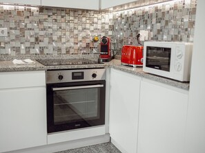A kitchen with white cabinets, a black oven, a red toaster, and a white microwave. - CITY CENTER GRAND SEA VIEW TERRACE by VACATIONY by Interhome (Porto)