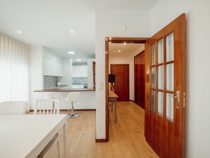 Une cuisine moderne avec des meubles blancs, un plan de travail en bois et un coin repas comprenant une table blanche et deux chaises.