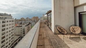 Terrassa al terrat amb vistes a edificis circumdants, zona d'estar amb dues cadires i una taula.