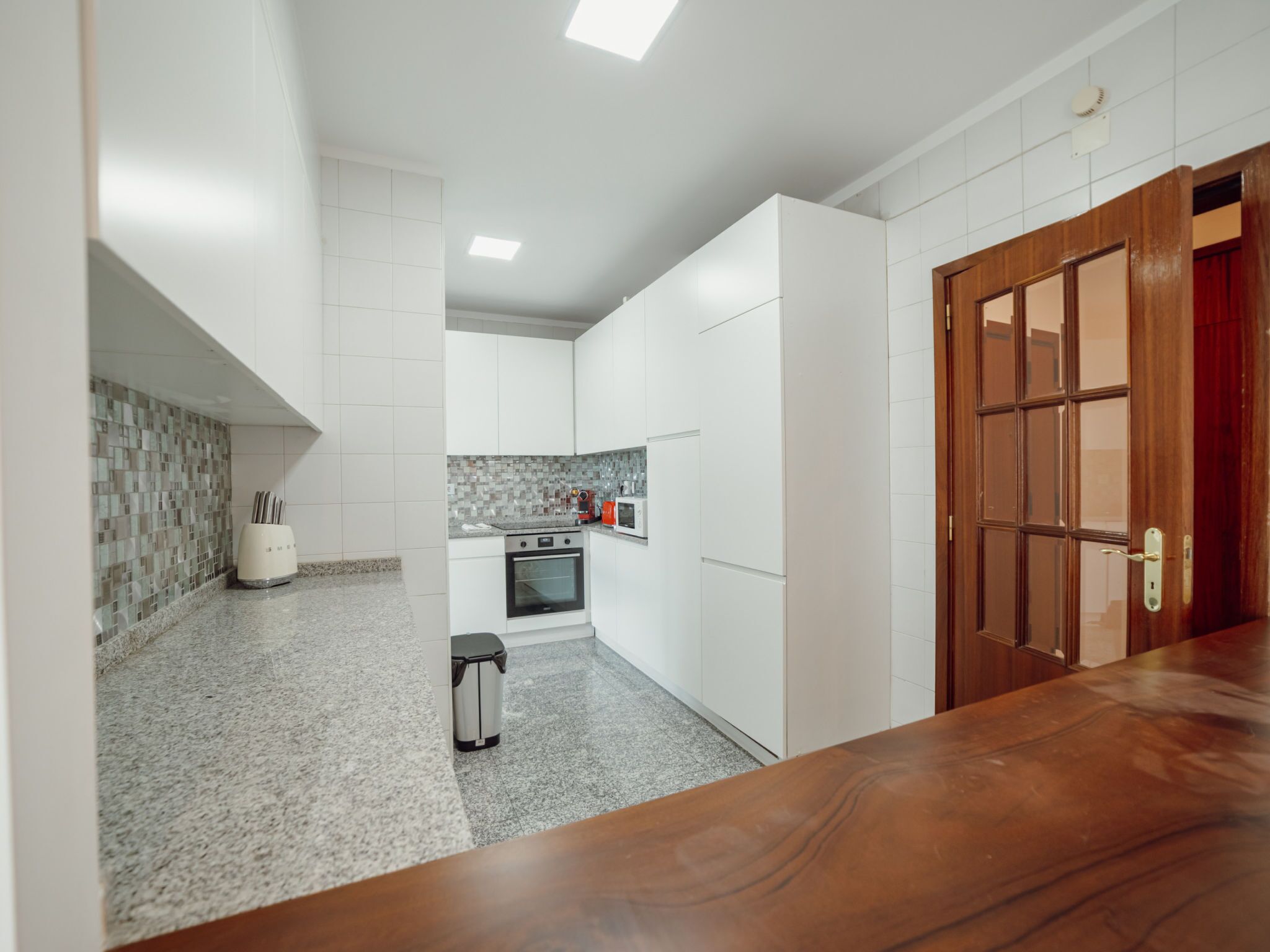 Una cocina moderna con armarios blancos, una encimera de granito y una puerta de madera.
