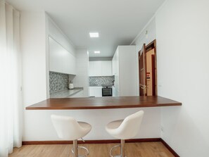 Eine moderne Küche mit weißen Schränken, einer Holz Arbeitsplatte und zwei weißen Barhocker.