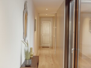 Um corredor com piso de madeira, uma porta no final e uma pequena mesa com uma planta à esquerda.