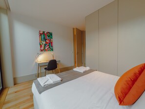 Ein Hotelzimmer mit einem Bett, einem Schreibtisch, einem Sessel und einem farbenfrohen, abstrakten Gemälde an der Wand.
