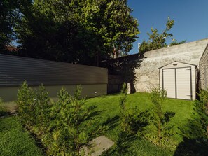 Un jardin arrière d’une maison, agrémenté d’un mur en pierre, d’un garage et d’une pelouse bien entretenue.
