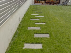 Ein Weg mit trittsteinförmigen Steinplatten führt zu einer Sitzgelegenheit mit Stühlen und Tischen.