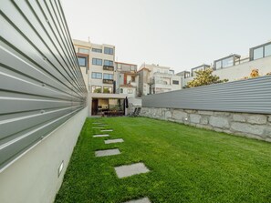 Une terrasse sur le toit avec une pelouse verdoyante, un mur de pierre et des bâtiments modernes en arrière-plan.