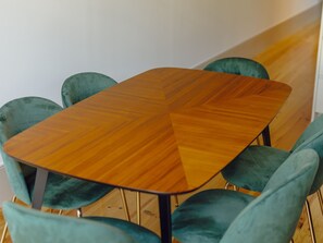 Uma mesa de madeira quadrada com padrão em chevron, rodeada por quatro cadeiras estofadas em tons de verde-água com pés de metal.