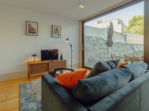 A modern living room with a sofa, a flat-screen TV, a coffee table, and a large window offering a view of the outdoors. - LEGACY OPORTO PREMIUM APARTMENT B by VACATIONY by Interhome (Porto)