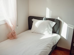 A single bed with white bedding, a dark headboard, and a window with sheer curtains. - CASA DAS ORQUIDEAS by VACATIONY by Interhome (Porto)