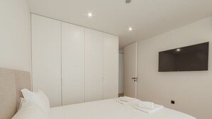 Un dormitorio moderno con una cama grande, un armario, un televisor de pantalla plana y una puerta que da a otra habitación.