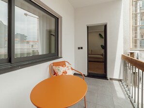 Ein Balkon mit einem einzelnen orangefarbenen Stuhl, einem Fenster und Blick auf Gebäude.