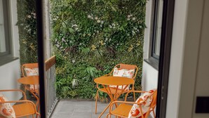 Un balcón con dos sillas anaranjadas y una mesa, rodeado de un exuberante jardín vertical verde.