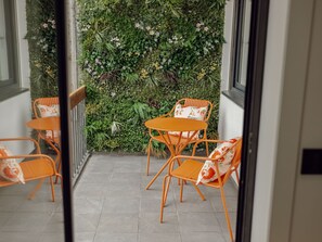 Ein Balkon mit zwei orangefarbenen Stühlen und einem Tisch, umgeben von einem üppigen vertikalen Garten.