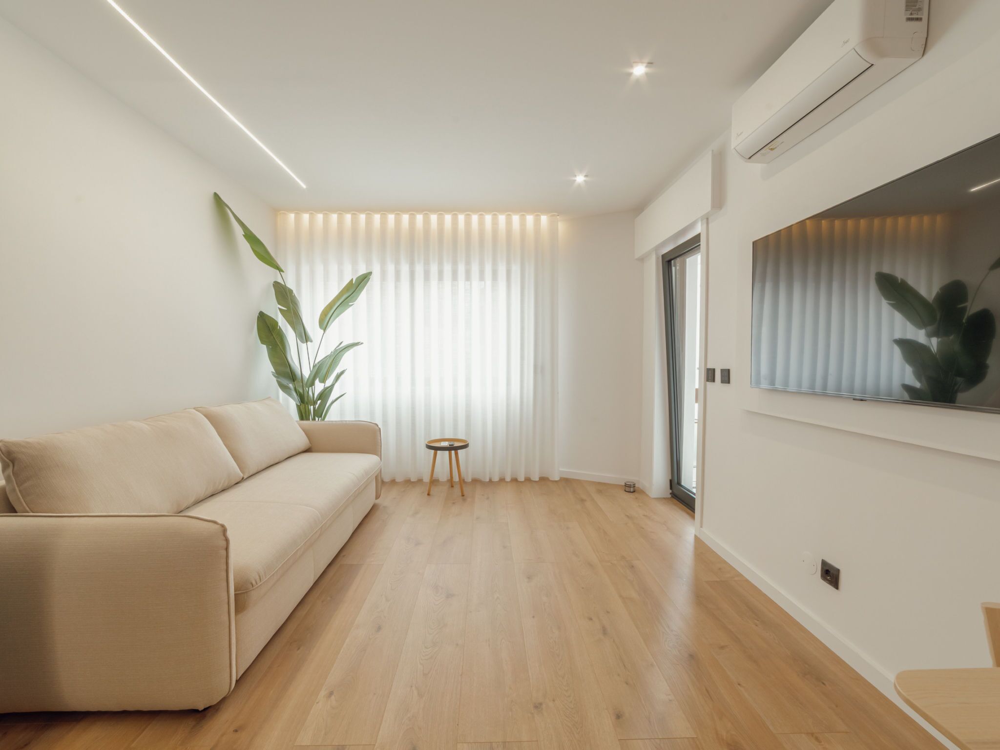 Ein modernes Wohnzimmer mit einem beige-farbenen Sofa, einem kleinen runden Tisch und einer großen Topfpflanze.