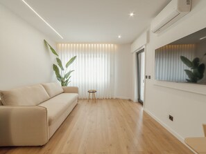 Ein modernes Wohnzimmer mit einem beige-farbenen Sofa, einem kleinen runden Tisch und einer großen Topfpflanze.