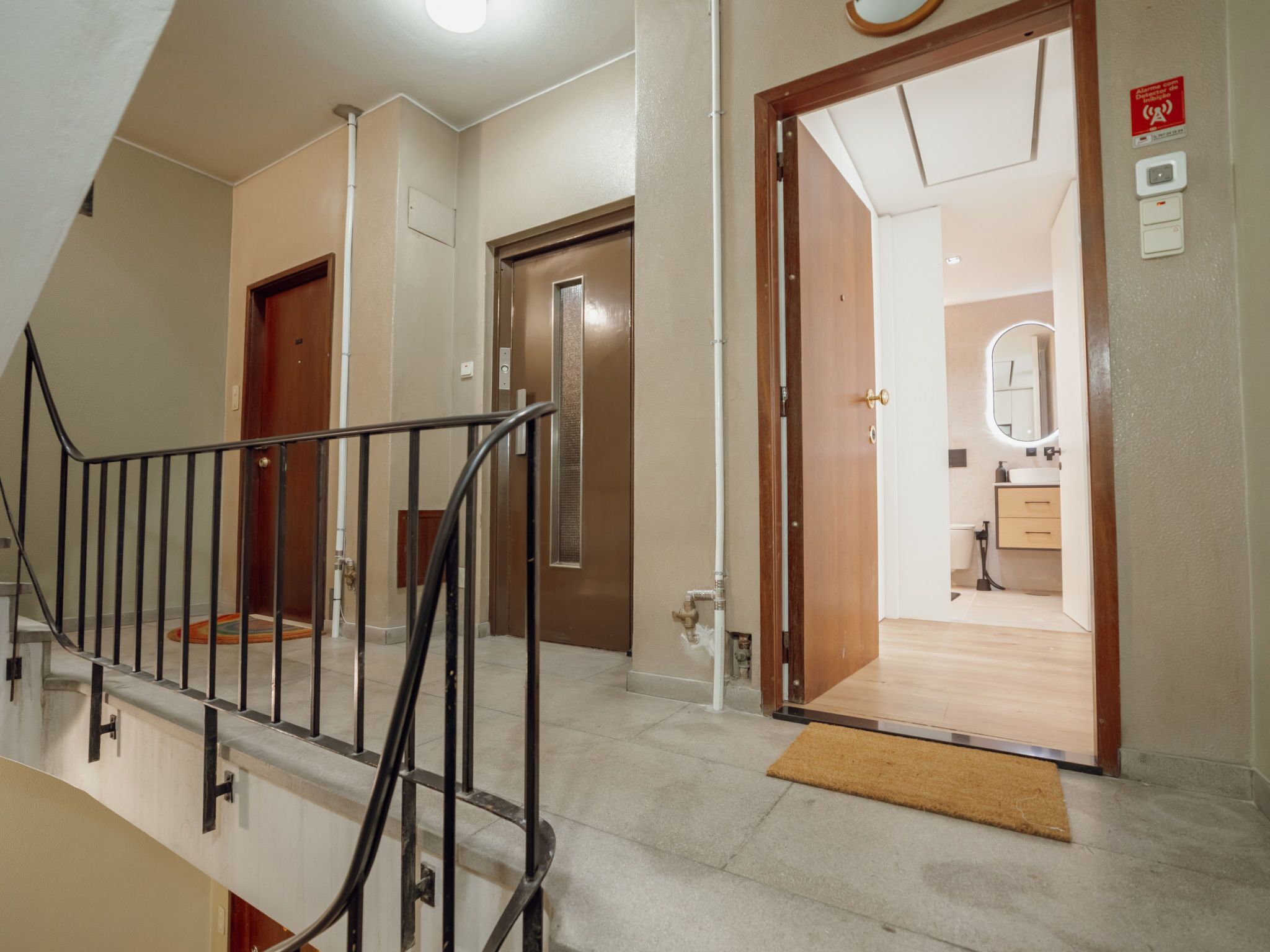 Ein Hotelgang mit Treppe, einer Tür zu einem Badezimmer und einem sichtbaren Alarmanlage.