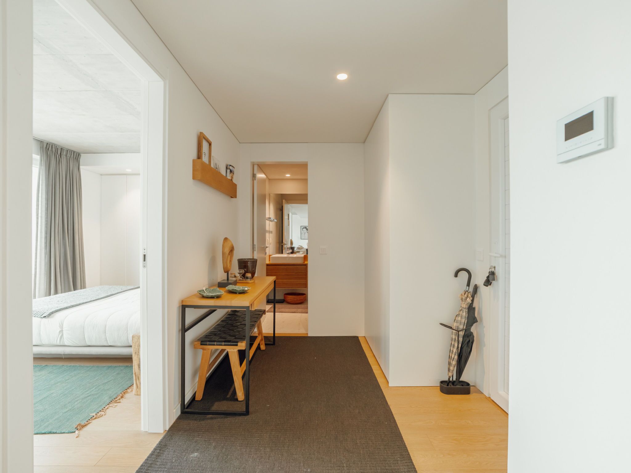 Ein Flur, der in ein Schlafzimmer führt, mit einem Bett, einem Tisch mit einem Stuhl und einem Kleiderständer mit einem Regenschirm.