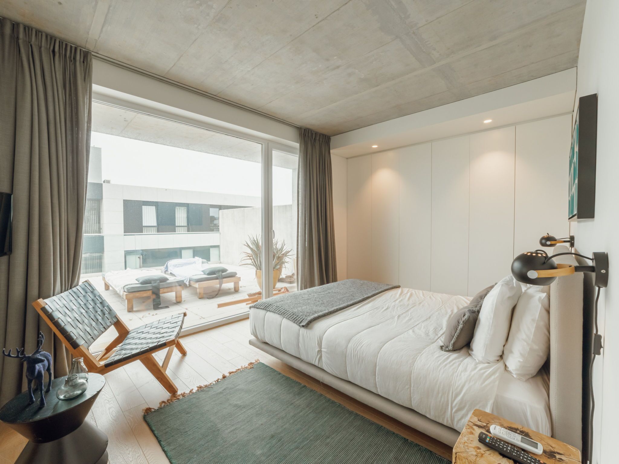 A modern bedroom with a bed, a desk, a chair, and a view of the outside.