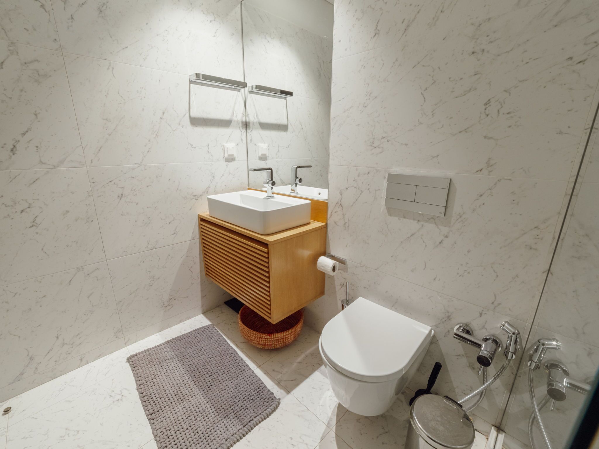 A modern bathroom with a white sink, wooden vanity, and a toilet.