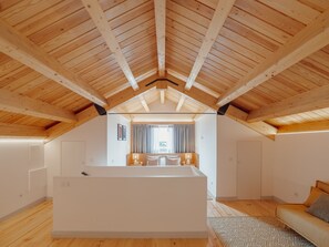 A spacious attic bedroom with a sloped wooden ceiling, a large bed, a sitting area with a sofa, and a view of the outside through a window. - Apartment  by Interhome (Porto)